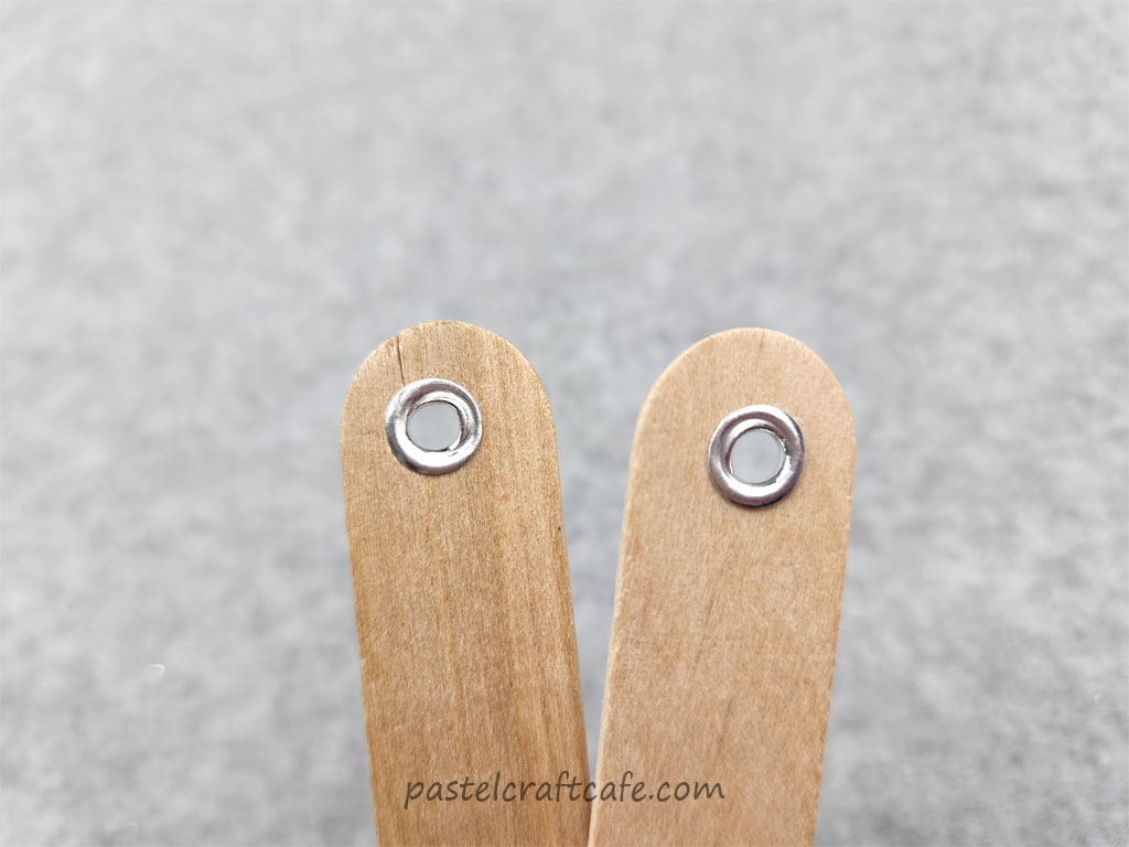 Warped silver eyelets pressed into the tops of popsicle sticks