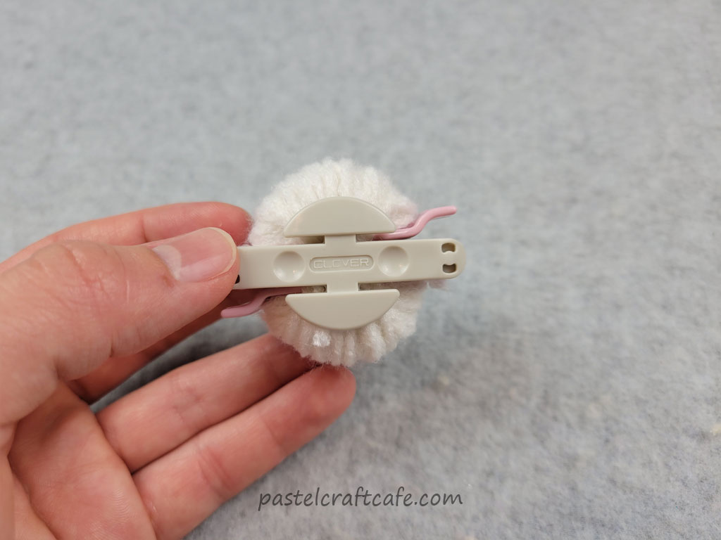 A small pom pom maker wound with white yarn