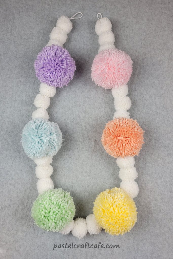 A finished pastel rainbow pom pom banner lying on a table