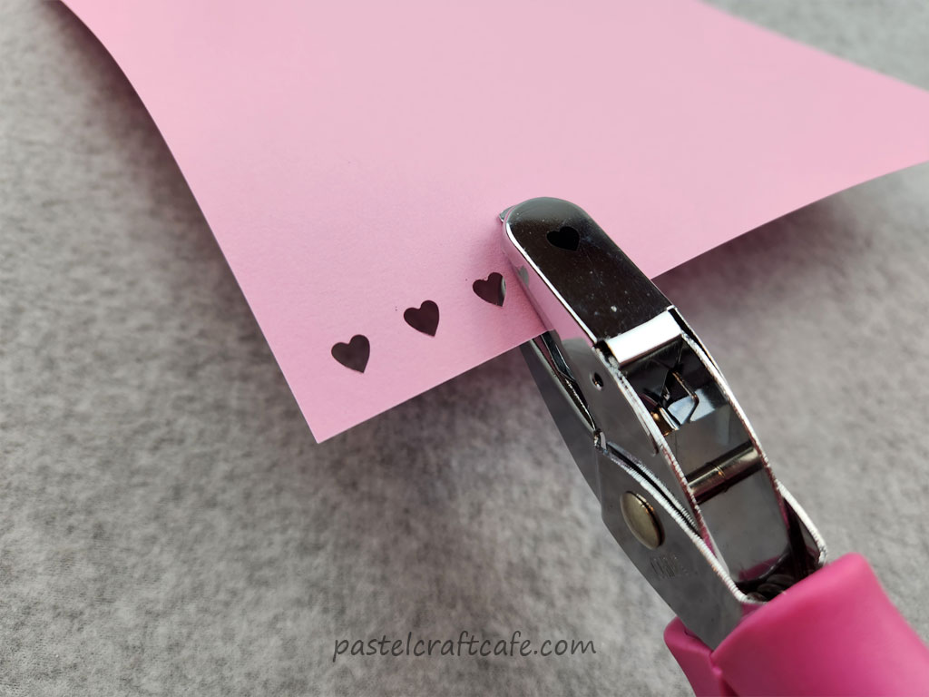 A heart hole punch that has punched holes in a piece of pink scrapbook paper