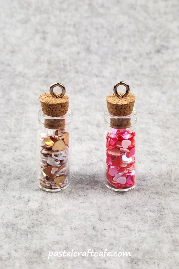 Two tiny bottle charms, each filled with a different mix of heart shaped confetti