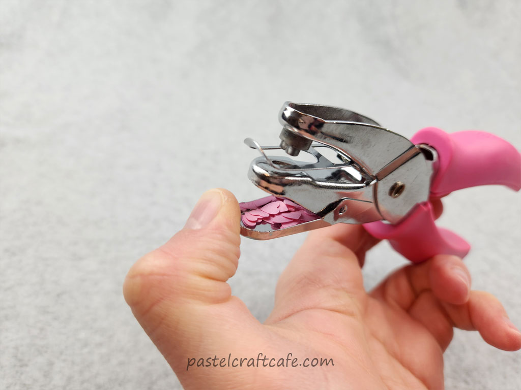 The open compartment of a heart hole punch, filled with tiny pink paper hearts