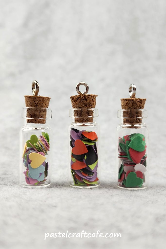 Three bottle charms filled with paper hearts in various different holiday colors
