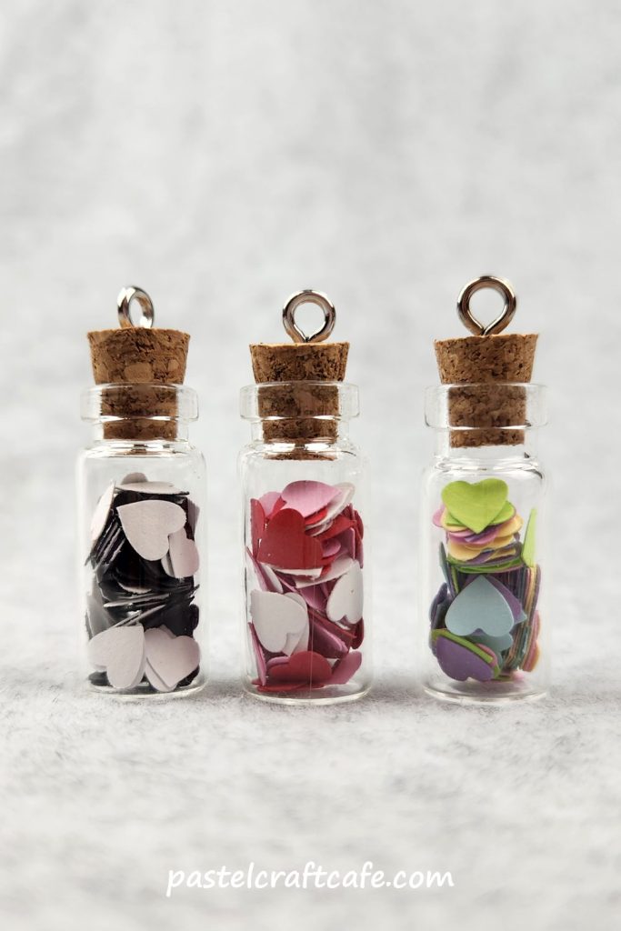 Three bottle charms filled with paper hearts in various different colors